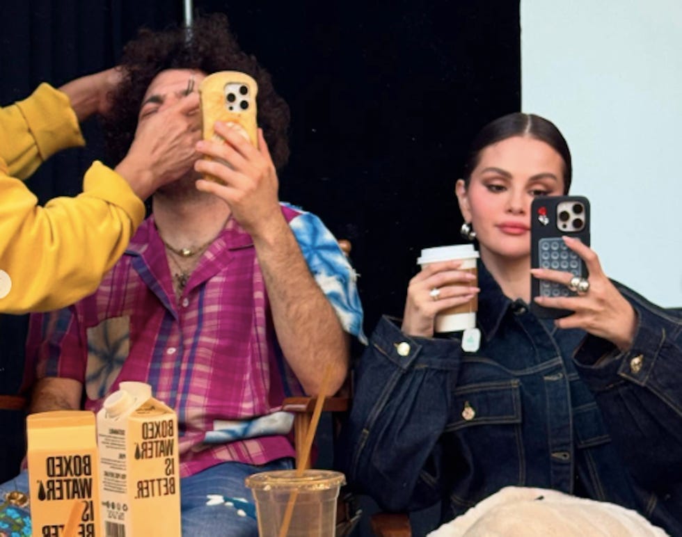 two individuals sitting together both holding phones while one receives attention